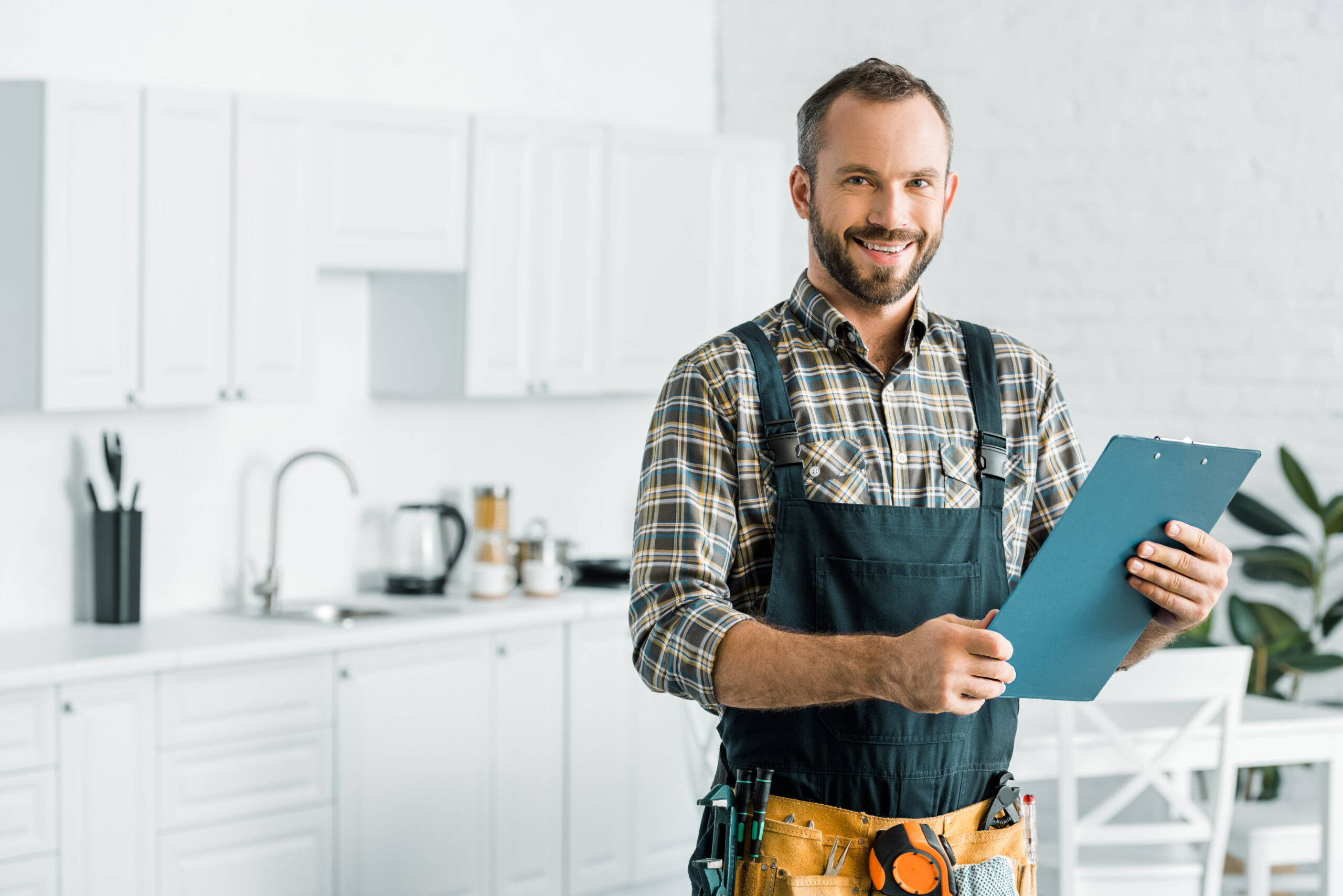 smiling handsome plumber holding clipboard and looking at camera smiling handsome plumber holding clipboard and looking at camera in kitchen